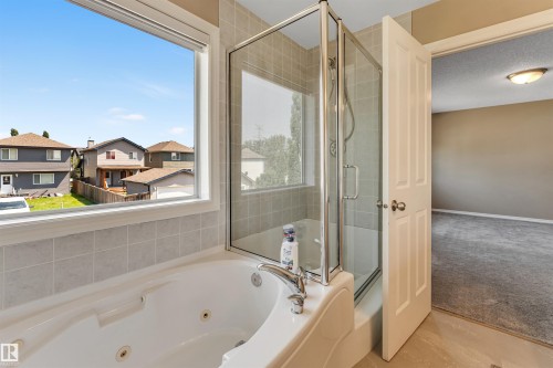 Soaking tub with integrated jets, glass-enclosed shower, light-toned wall tile, and a large window - 121 64 Street Sw, Edmonton, AB - Indoor Photo Showing Bathroom