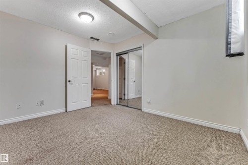 Carpeted room featuring light gray walls, white trim, a flush-mount ceiling light, and a mirrored closet door - 121 64 Street Sw, Edmonton, AB - Indoor Photo Showing Other Room