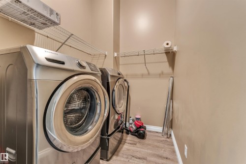 Dedicated laundry area featuring a front-load washer and dryer, wire shelving, and wood-finish flooring - 121 64 Street Sw, Edmonton, AB - Indoor Photo Showing Laundry Room