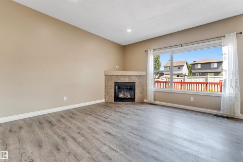 Bright living area featuring wood-finish flooring, a contemporary fireplace with a tiled surround, a large picture window, and recessed lighting - 121 64 Street Sw, Edmonton, AB - Indoor Photo Showing Living Room With Fireplace