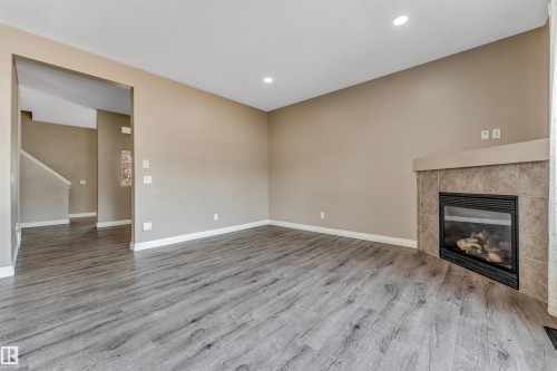 Spacious living area featuring wood-finish flooring, a tiled fireplace with mantel, recessed lighting, and neutral wall tones - 121 64 Street Sw, Edmonton, AB - Indoor With Fireplace