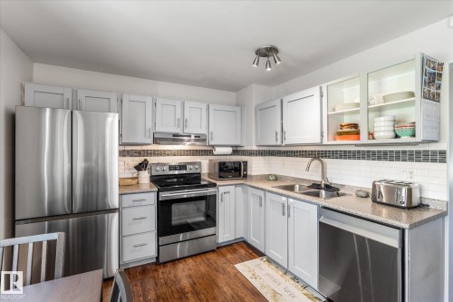 Kitchen featuring stainless steel appliances, light gray cabinetry, speckled countertops, a subway tile backsplash with accent band, and wood-finish flooring - 4718 35 Avenue Nw, Edmonton, AB - Indoor Photo Showing Kitchen With Double Sink