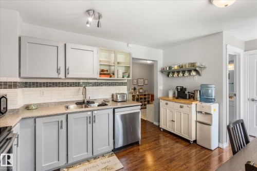 Kitchen featuring light gray cabinetry, a stainless steel dishwasher, a single basin sink with a high-arc faucet, white subway tile backsplash with a decorative accent, and wood-finish flooring - 4718 35 Avenue Nw, Edmonton, AB - Indoor Photo Showing Kitchen With Double Sink