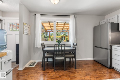 Dining area with wood-finish flooring, light grey wall paint, and a window overlooking a covered patio structure - 4718 35 Avenue Nw, Edmonton, AB - Indoor