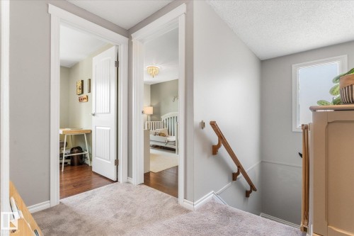 Carpeted hallway featuring a wooden handrail, neutral wall tones, and white trim - 4718 35 Avenue Nw, Edmonton, AB - Indoor Photo Showing Other Room