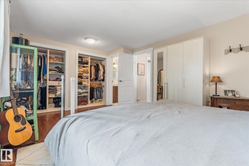 Bedroom featuring hardwood-style flooring, two open closets with built-in shelving, a set of white built-in wardrobes, and a door opening to an additional room - 4718 35 Avenue Nw, Edmonton, AB - Indoor Photo Showing Bedroom