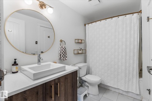 Bathroom featuring a vessel sink atop a wood-finish vanity with gold-tone hardware, a round framed mirror, and a full bathtub with a shower curtain - 4718 35 Avenue Nw, Edmonton, AB - Indoor Photo Showing Bathroom