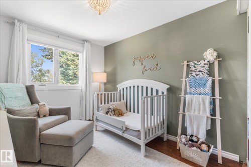 Bright room featuring a window with exterior tree scenery, light green accent wall, wood-finish flooring, and a decorative ceiling fixture - 4718 35 Avenue Nw, Edmonton, AB - Indoor Photo Showing Bedroom