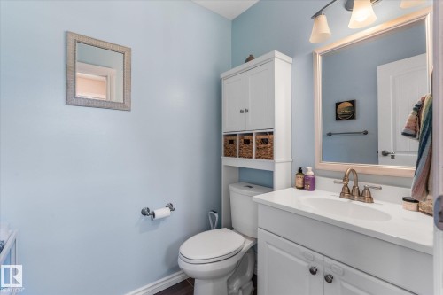 Vanity with integrated sink and brass-finish faucet, framed mirror, and over-toilet built-in cabinetry with woven storage bins - 4718 35 Avenue Nw, Edmonton, AB - Indoor Photo Showing Bathroom