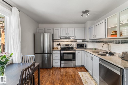 Kitchen featuring wood-finish flooring, light cabinetry, stainless steel appliances, a white subway tile backsplash, and track lighting - 4718 35 Avenue Nw, Edmonton, AB - Indoor Photo Showing Kitchen With Double Sink
