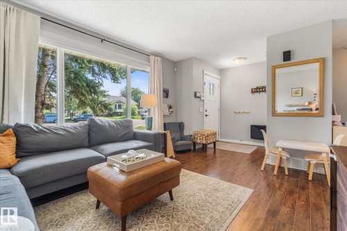Living area featuring large picture windows, wood-finish flooring, a neutral color palette, recessed lighting, and a front entry door with decorative glass inserts - 4718 35 Avenue Nw, Edmonton, AB - Indoor Photo Showing Living Room