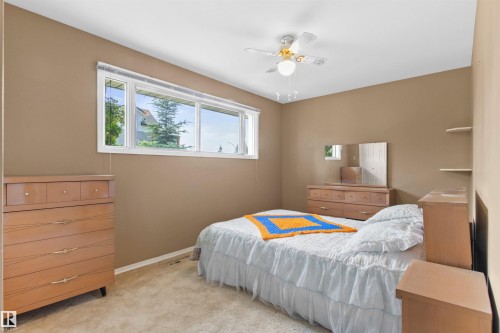 Spacious room featuring a multi-pane window, neutral-toned walls, light-colored carpeting, a ceiling fan with integrated lighting, and built-in shelving - 12316 135 Avenue Nw, Edmonton, AB - Indoor Photo Showing Bedroom