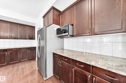Kitchen featuring wood-finish flooring, dark wood cabinetry, light-colored countertops, a white tile backsplash, and a stainless steel refrigerator - 