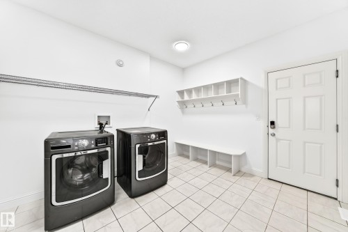 Utility room featuring a white paneled door, built-in shelving with coat hooks, a built-in bench, and light-toned tile flooring - 1663 Rutherford Road Sw, Edmonton, AB - Indoor Photo Showing Laundry Room