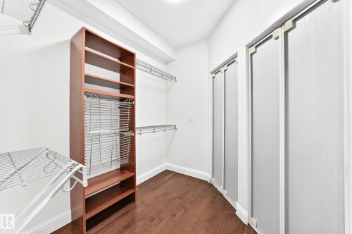 Walk-in closet featuring wood-finish flooring, built-in shelving, wire rack organizers, chrome hanging rods, and bi-fold closet doors - 1663 Rutherford Road Sw, Edmonton, AB - Indoor