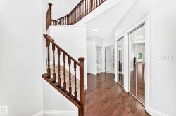 Two-story staircase with dark wood balusters and handrails, complemented by wood-finish flooring, white walls, and mirrored closet doors - 
