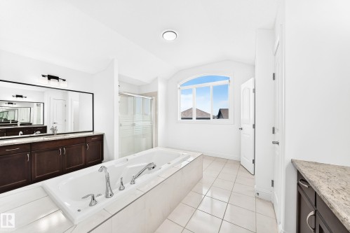 Spacious bathroom featuring a built-in soaking tub, separate glass-enclosed shower, dual vanities with dark wood cabinetry, and an arched window - 1663 Rutherford Road Sw, Edmonton, AB - Indoor