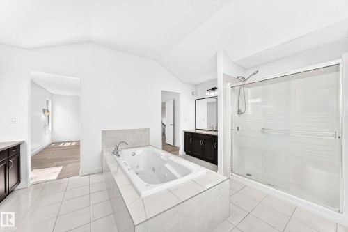 Bathroom featuring a jetted soaking tub with tiled surround, a glass-enclosed shower with sliding door, and a dual vanity with dark wood-finish cabinetry and a framed mirror - 1663 Rutherford Road Sw, Edmonton, AB - Indoor Photo Showing Bathroom