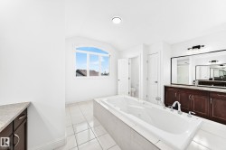 Spacious bathroom featuring a built-in soaking tub with chrome fixtures, dual vanity with dark wood cabinetry and light-toned countertops, and an arched window - 