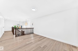 Upper-level landing featuring light wood-finish flooring, white walls, and a dark wood staircase railing - 