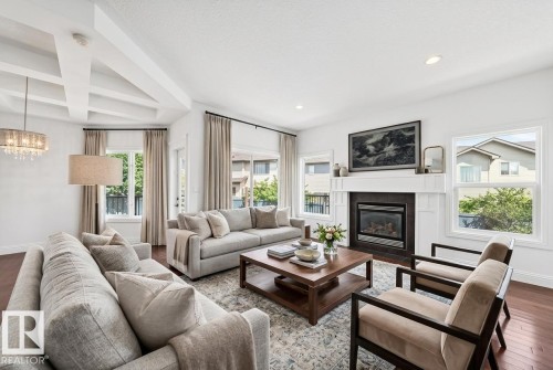 Spacious living room featuring rich wood-finish flooring, a coffered ceiling, and a prominent fireplace with a white mantel and dark tile surround - 1663 Rutherford Road Sw, Edmonton, AB - Indoor Photo Showing Living Room With Fireplace