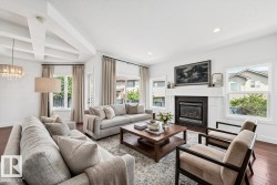 Spacious living room featuring rich wood-finish flooring, a coffered ceiling, and a prominent fireplace with a white mantel and dark tile surround - 