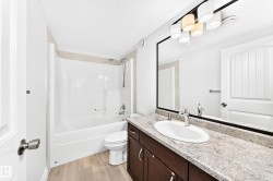 Bathroom featuring a vanity with a light-toned speckled countertop, an undermount sink with chrome fixtures, a large framed mirror, and a multi-bulb vanity light - 