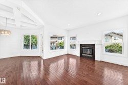 Bright living area featuring wood-finish flooring, multiple large windows, a central fireplace with a dark surround and white mantel, a decorative coffered ceiling detail, and a contemporary chandelier - 