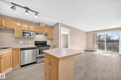 Kitchen and living area featuring wood-finish flooring - #317 245 Edwards Dr Sw, Edmonton, AB - Indoor Photo Showing Kitchen With Stainless Steel Kitchen