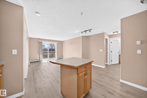 Open-concept living space featuring wood-finish flooring, a kitchen island with light-toned countertop, and a sliding glass door to a balcony - #317 245 Edwards Dr Sw, Edmonton, AB - Indoor Photo Showing Other Room