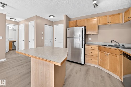 Kitchen featuring wood-finish cabinetry, stainless steel refrigerator, and a double basin sink - #317 245 Edwards Dr Sw, Edmonton, AB - Indoor Photo Showing Kitchen With Double Sink