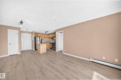 Open-concept living area featuring wood-finish flooring, a kitchen with light wood cabinetry, a stainless steel refrigerator, and a freestanding island - 