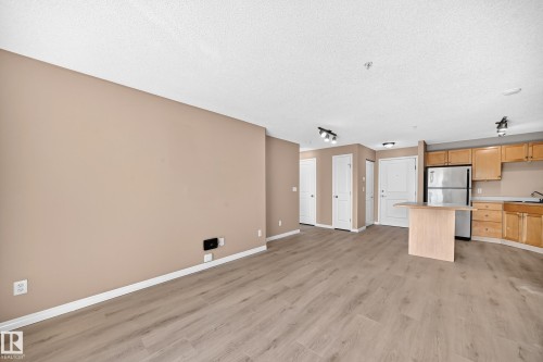 Open-concept living space featuring wood-finish flooring throughout, light beige wall tones, and white baseboards - #317 245 Edwards Dr Sw, Edmonton, AB - Indoor Photo Showing Kitchen