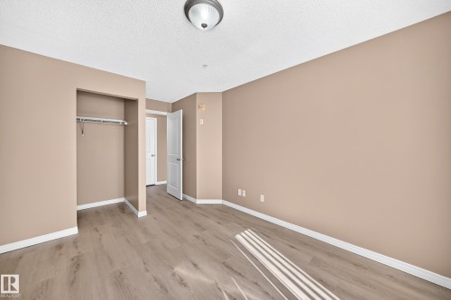 Spacious room featuring wood-finish flooring, neutral-toned walls, white trim, an open closet with a hanging rod, and a ceiling-mounted light fixture - #317 245 Edwards Dr Sw, Edmonton, AB - Indoor Photo Showing Other Room