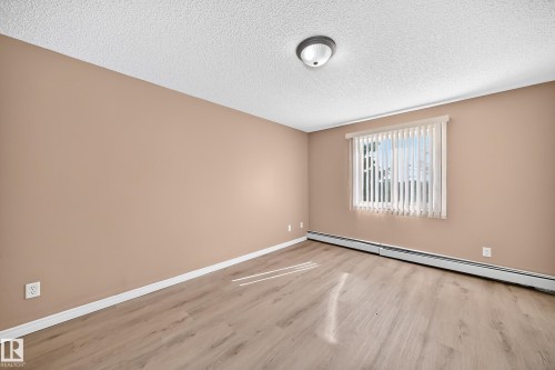 Room featuring wood-finish flooring, a window with vertical blinds, a baseboard heater, and a flush-mount ceiling light - #317 245 Edwards Dr Sw, Edmonton, AB - Indoor Photo Showing Other Room