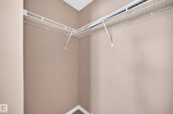 Corner closet featuring wire shelving and hanging rods, neutral wall tones, and white baseboards - 