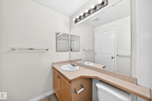 Neutral-toned bathroom featuring a wood-finish vanity with a single basin sink and a light-colored countertop - #317 245 Edwards Dr Sw, Edmonton, AB - Indoor Photo Showing Bathroom