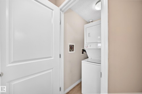 Dedicated laundry closet featuring a white stacked washer and dryer unit, wood-finish flooring, and light-toned walls - #317 245 Edwards Dr Sw, Edmonton, AB - Indoor Photo Showing Laundry Room