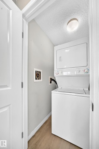 Dedicated laundry closet featuring a stacked white washer and dryer, wood-finish flooring, and a flush-mount ceiling light - #317 245 Edwards Dr Sw, Edmonton, AB - Indoor Photo Showing Laundry Room