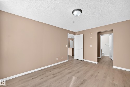 Neutral tone walls, wood-finish flooring, white trim, and a semi-flush ceiling light - #317 245 Edwards Dr Sw, Edmonton, AB - Indoor Photo Showing Other Room