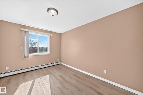 Windowed room featuring wood-finish flooring, neutral wall tones, baseboard heating, and a ceiling-mounted light fixture - #317 245 Edwards Dr Sw, Edmonton, AB - Indoor Photo Showing Other Room