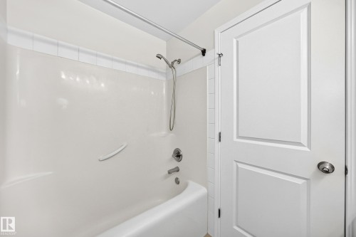 Bathtub and shower combination featuring a white surround, chrome fixtures, and a shower curtain rod - #317 245 Edwards Dr Sw, Edmonton, AB - Indoor Photo Showing Bathroom