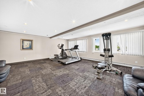 Spacious interior room featuring patterned carpet flooring, recessed lighting, and multiple windows with vertical blinds - #317 245 Edwards Dr Sw, Edmonton, AB - Indoor Photo Showing Gym Room