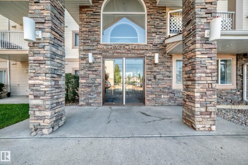 Stone veneer exterior with arched window accent, dual glass entry doors, and concrete walkway - #317 245 Edwards Dr Sw, Edmonton, AB - Outdoor With Balcony