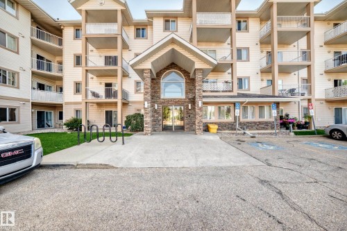 Multi-story residential building featuring a stone-clad entry, exterior balconies with white railings, and ground-level patios - #317 245 Edwards Dr Sw, Edmonton, AB - Outdoor With Balcony With Facade