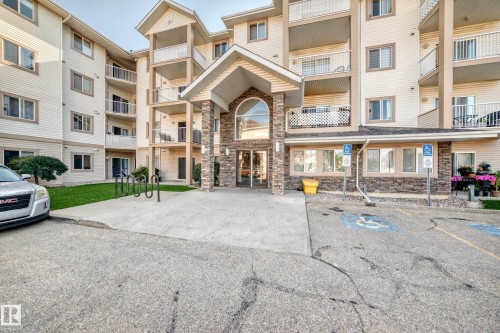 Multi-story building with a covered entry featuring stone veneer columns and an arched window - #317 245 Edwards Dr Sw, Edmonton, AB - Outdoor With Balcony With Facade