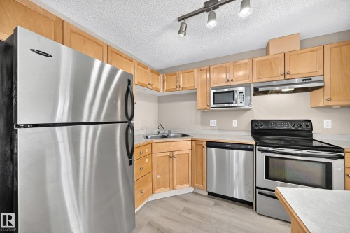 Kitchen featuring stainless steel appliances, light wood cabinetry, light countertops, and wood-finish flooring - #317 245 Edwards Dr Sw, Edmonton, AB - Indoor Photo Showing Kitchen With Stainless Steel Kitchen With Double Sink