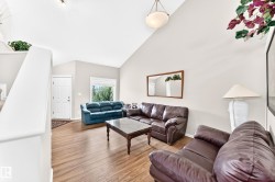 Vaulted ceilings over a spacious living area featuring wood-finish flooring, a white front entry door, and a bright window with exterior tree views - 