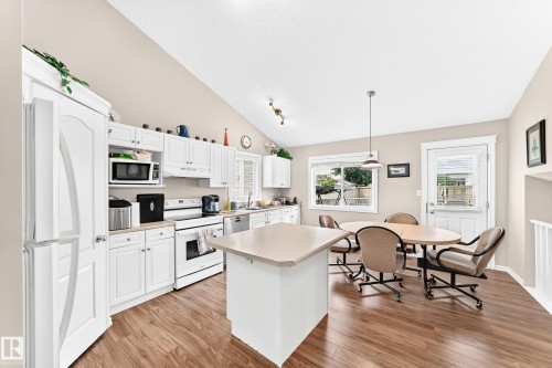 Open-concept kitchen and dining area featuring vaulted ceilings, wood-finish flooring, white cabinetry, a kitchen island, and a glass-paneled back door - 3226 30 Avenue Nw, Edmonton, AB - Indoor Photo Showing Kitchen With Double Sink