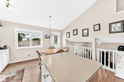 Kitchen featuring vaulted ceilings, white cabinetry, wood-finish flooring, a pendant light fixture, and a window with a backyard outlook - 